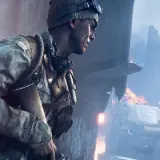 Żołnierz w czapce i goglach, gotowy do akcji w grze fps. W tle płonące ruiny i dym.
