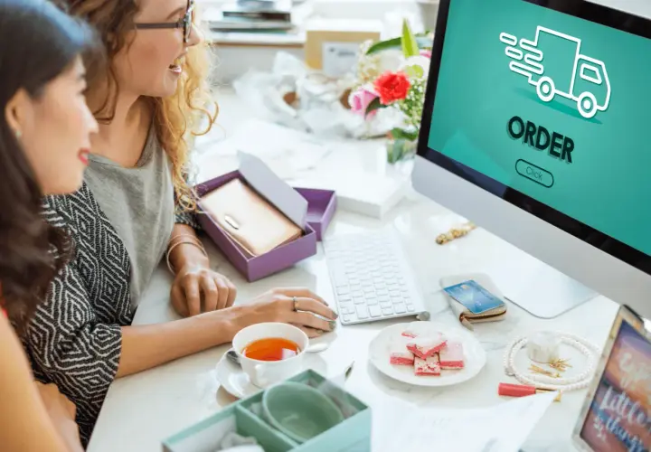 Dwie kobiety przeglądają komputer, na ekranie widnieje napis "ORDER" i ikona ciężarówki. To pokazuje, jak działa preorder.