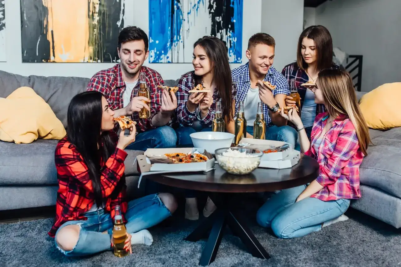 Grupa przyjaciół cieszy się pizzą i napojami, przygotowując się do wieczoru pełnego śmiechu i gry planszowe.