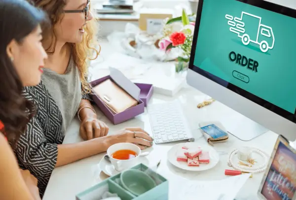 Dwie kobiety przeglądają komputer, na ekranie widnieje napis "ORDER" i ikona ciężarówki. To pokazuje, jak działa preorder.